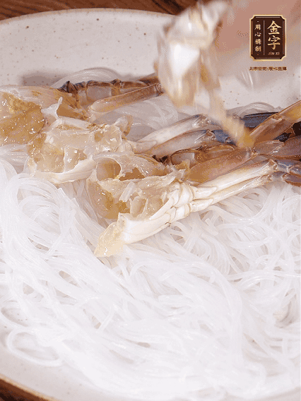 盤底墊上粉絲，擺上梭子蟹、火腿片，撒姜粒，淋上蒸魚豉油、花雕酒調(diào)味腌制15分鐘